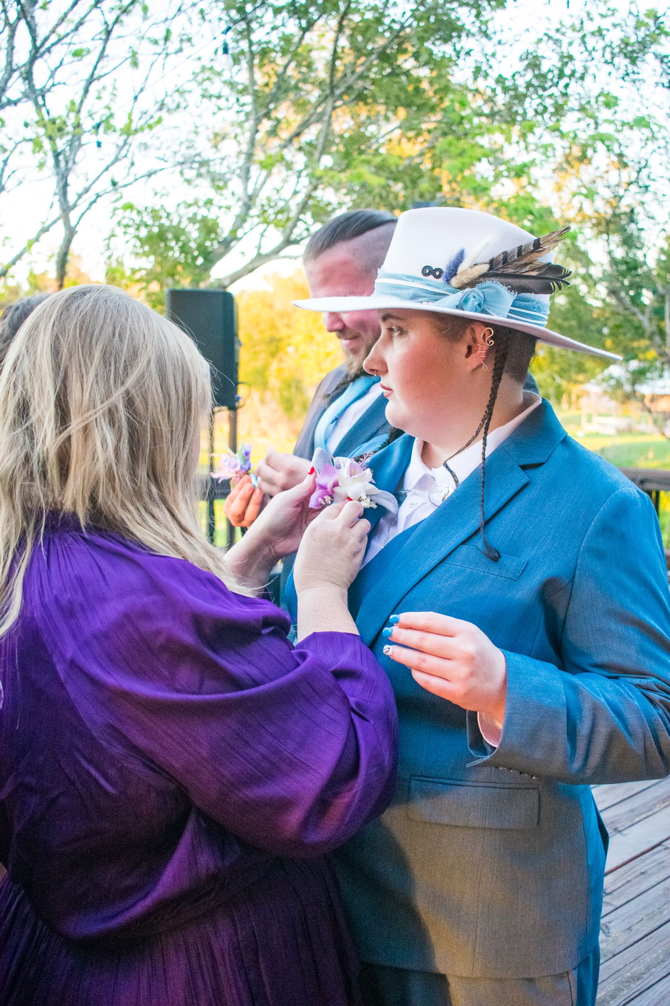 Close-up of purple corsage being pinned on blue suit at outdoor event.