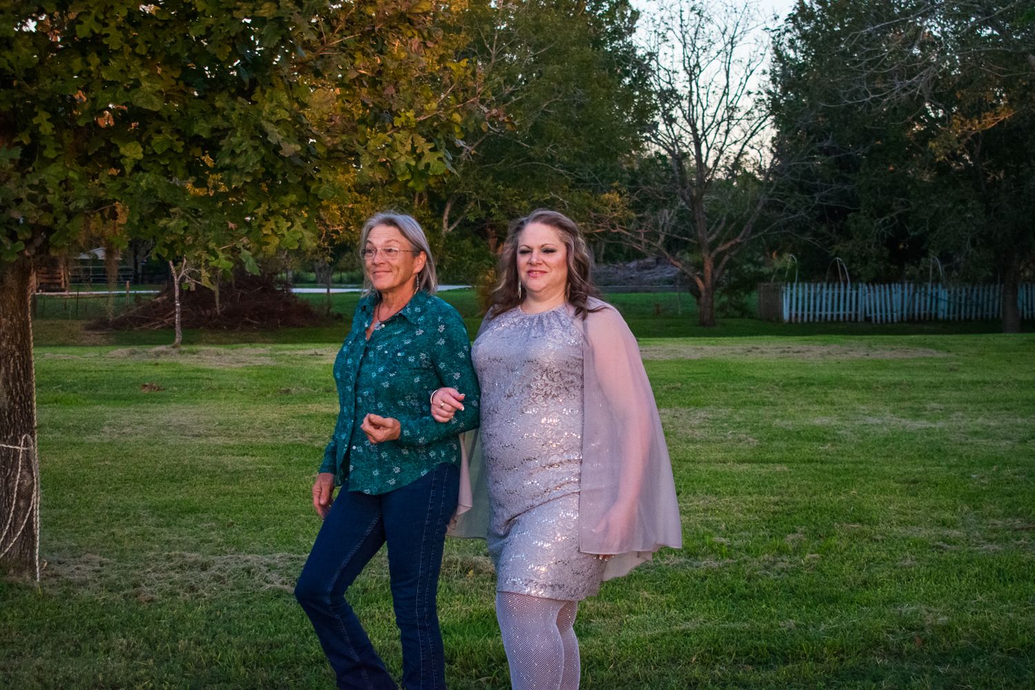 Two attendees share a joyful dance moment on a grassy lawn during an outdoor event at sunset.