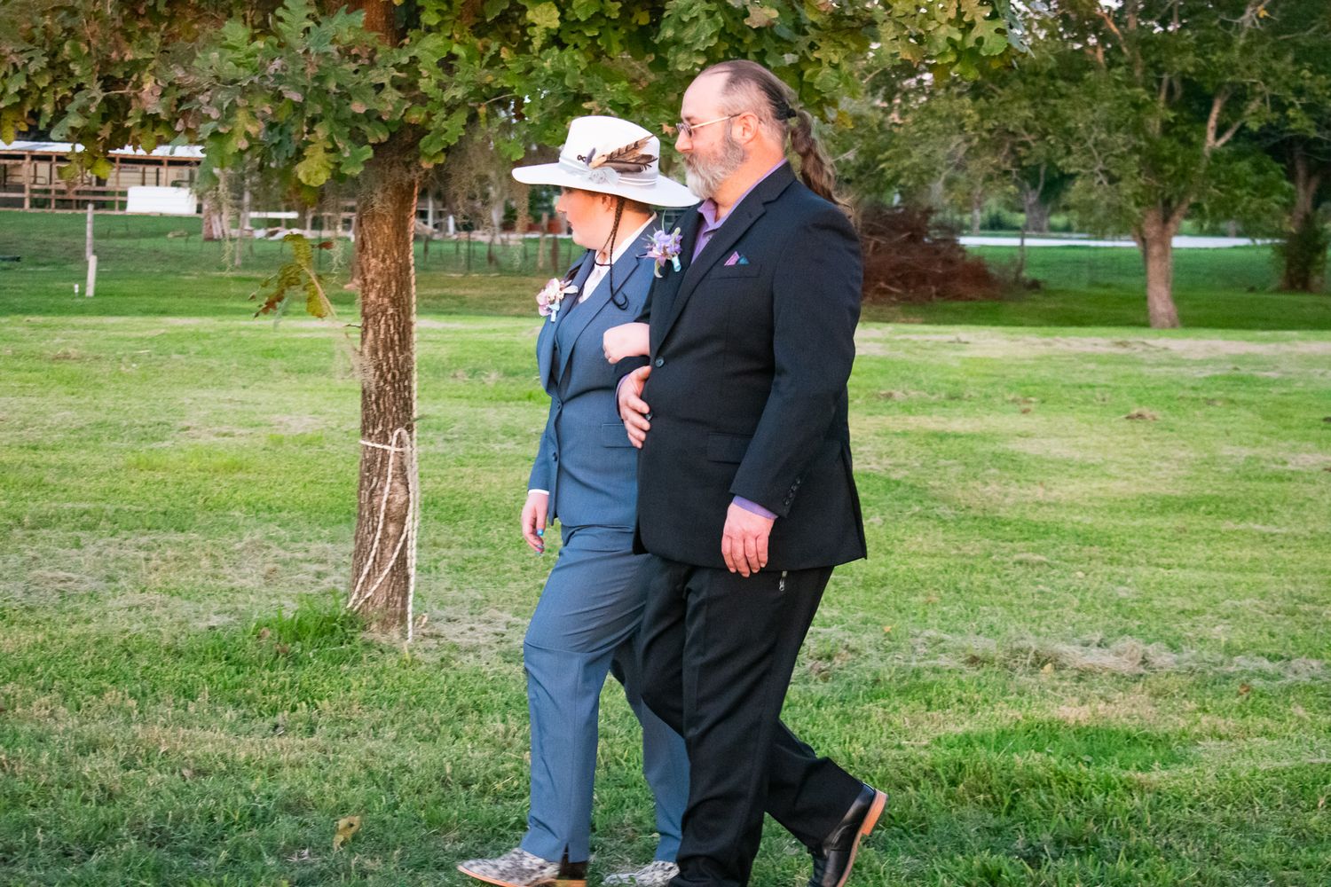 A couple takes a stroll together through a park wearing formal attire.