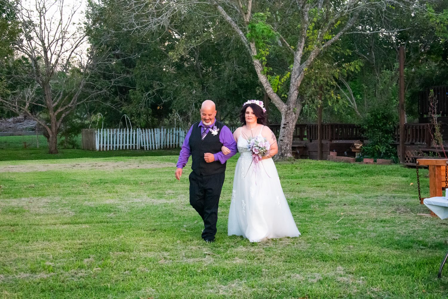 A couple walks together on green grass during their outdoor wedding ceremony.