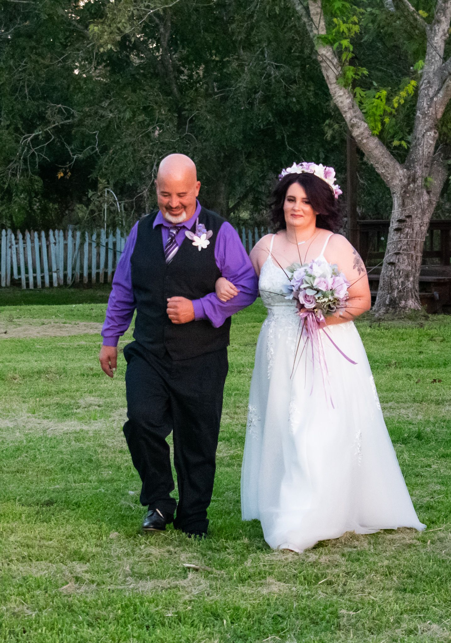 A couple in coordinated purple and white wedding attire walks together on their special day.