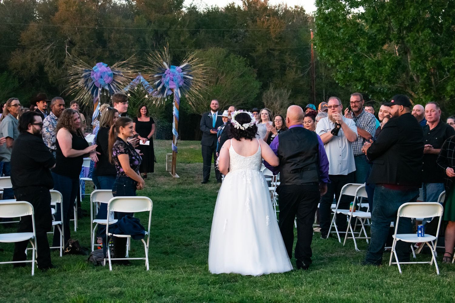 An outdoor wedding ceremony with guests seated in white chairs under colorful decorative star bursts.