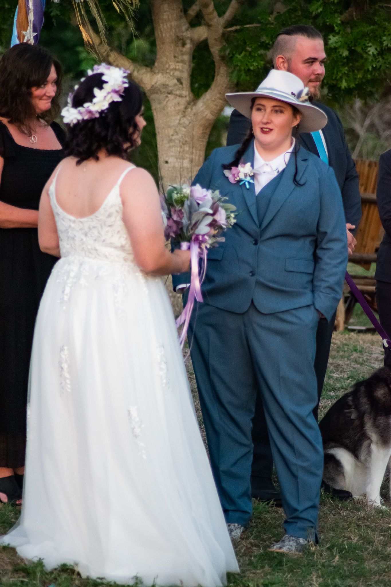 A wedding moment captured outdoors with one participant in a white gown and another in a blue suit.