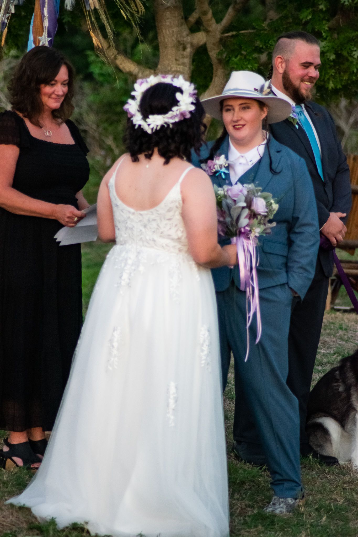 An intimate outdoor wedding scene with attendees and a black and white husky dog in the background.
