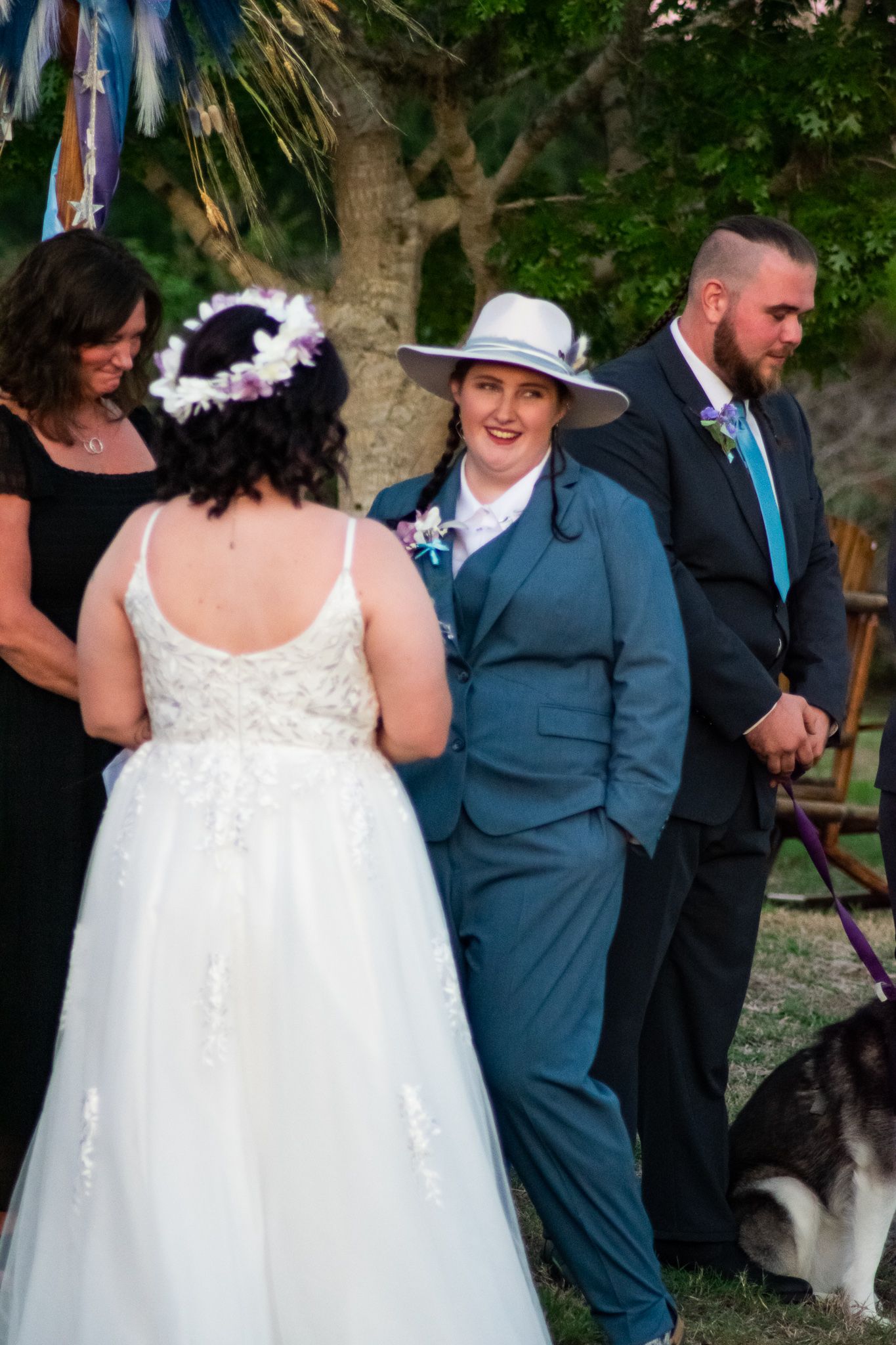 A wedding ceremony with attendees in formal attire gathered under trees with decorative ribbons.