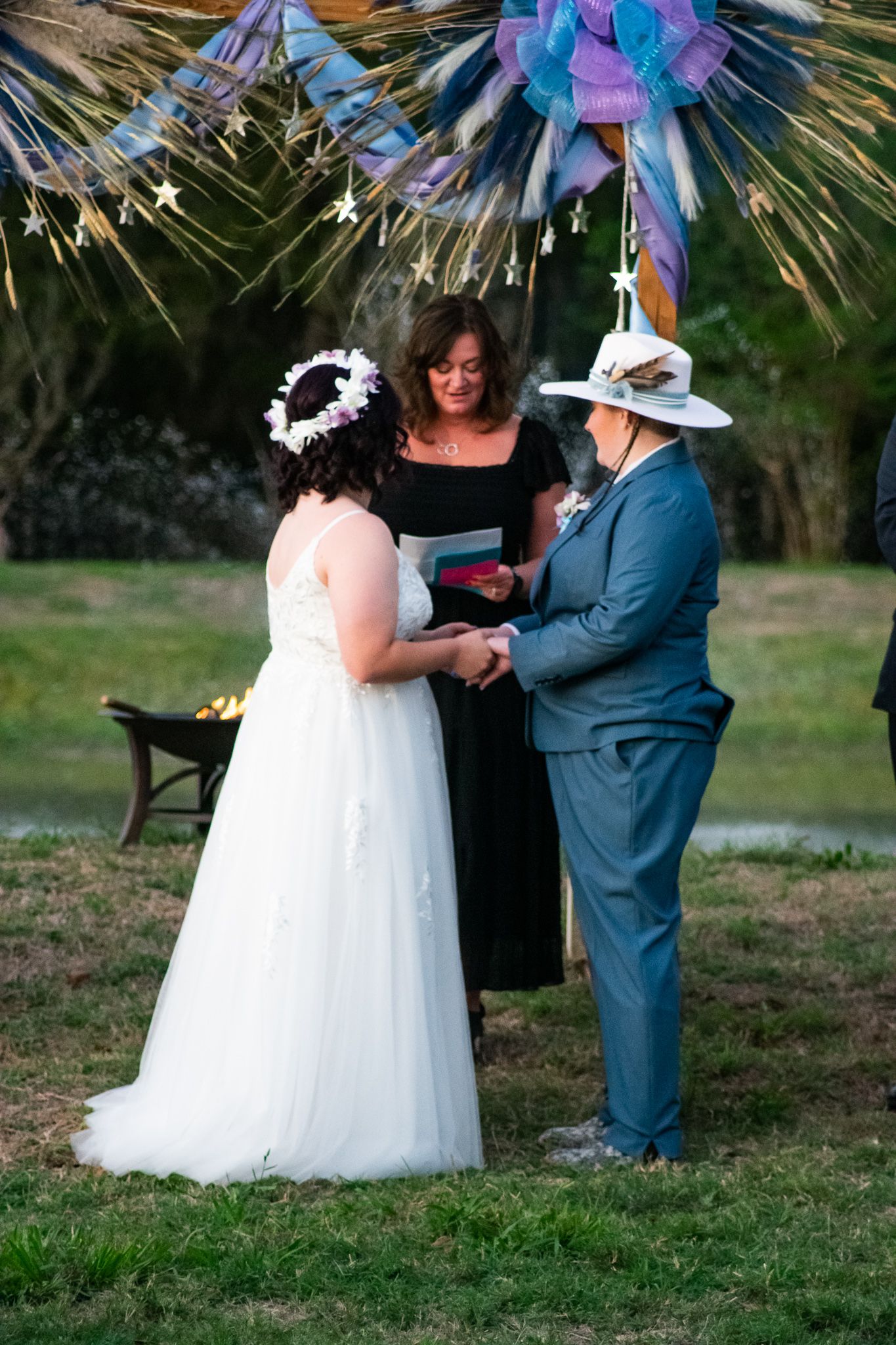 An outdoor wedding ceremony under decorative stars and ribbons with three people at the altar.
