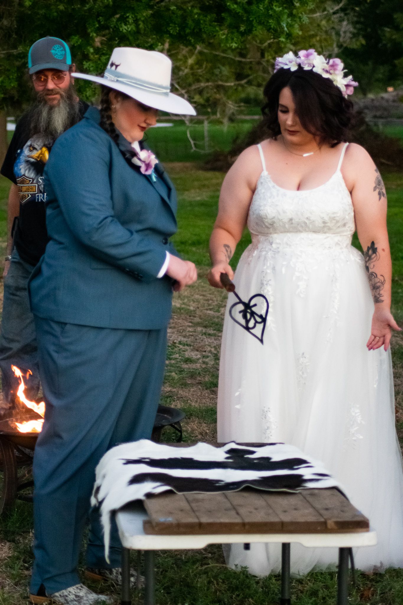 A couple performs a unity ceremony at their outdoor wedding with a wooden table displaying ceremonial items.