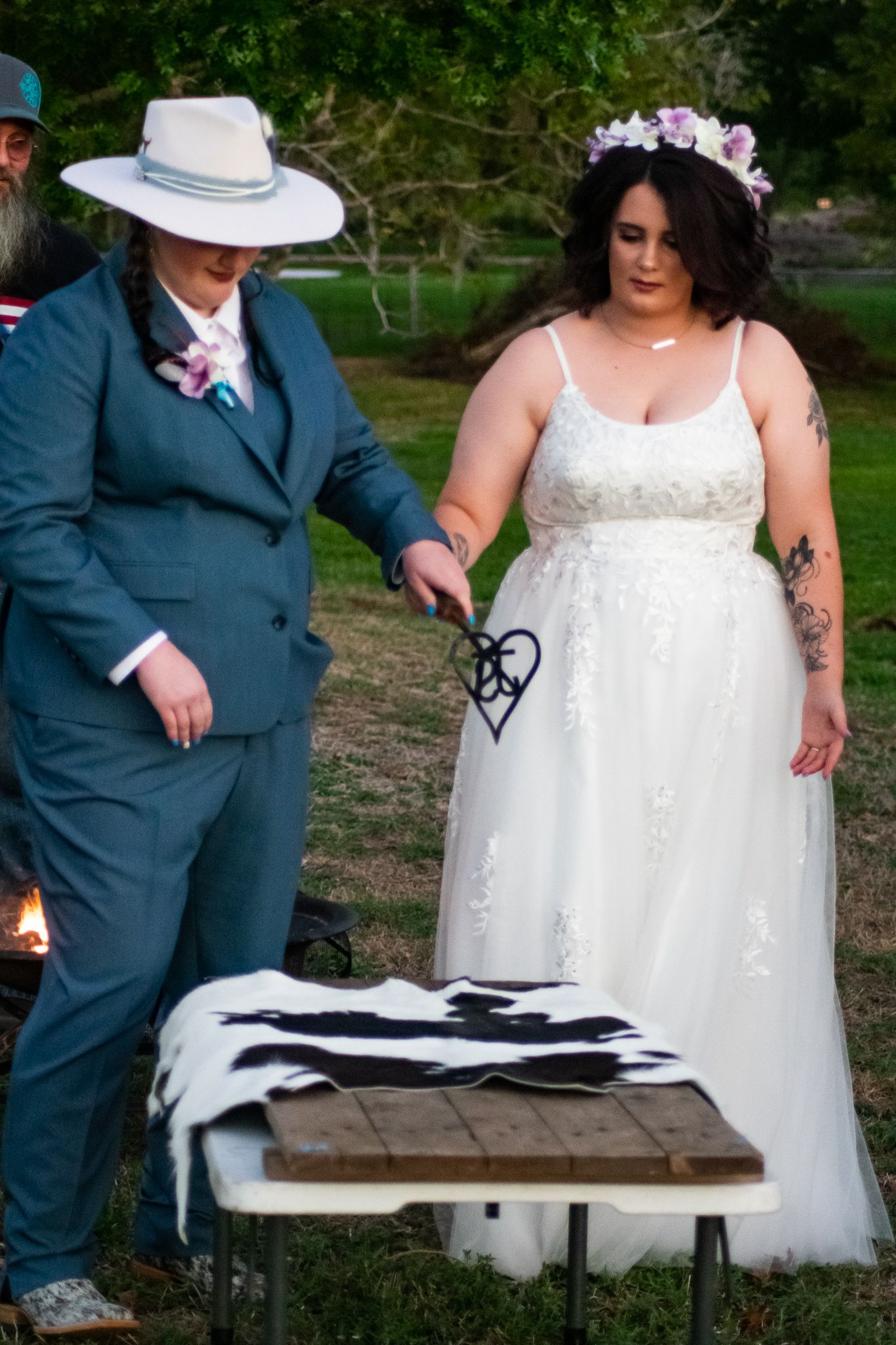 Two people stand at a wooden table during an outdoor wedding ceremony.
