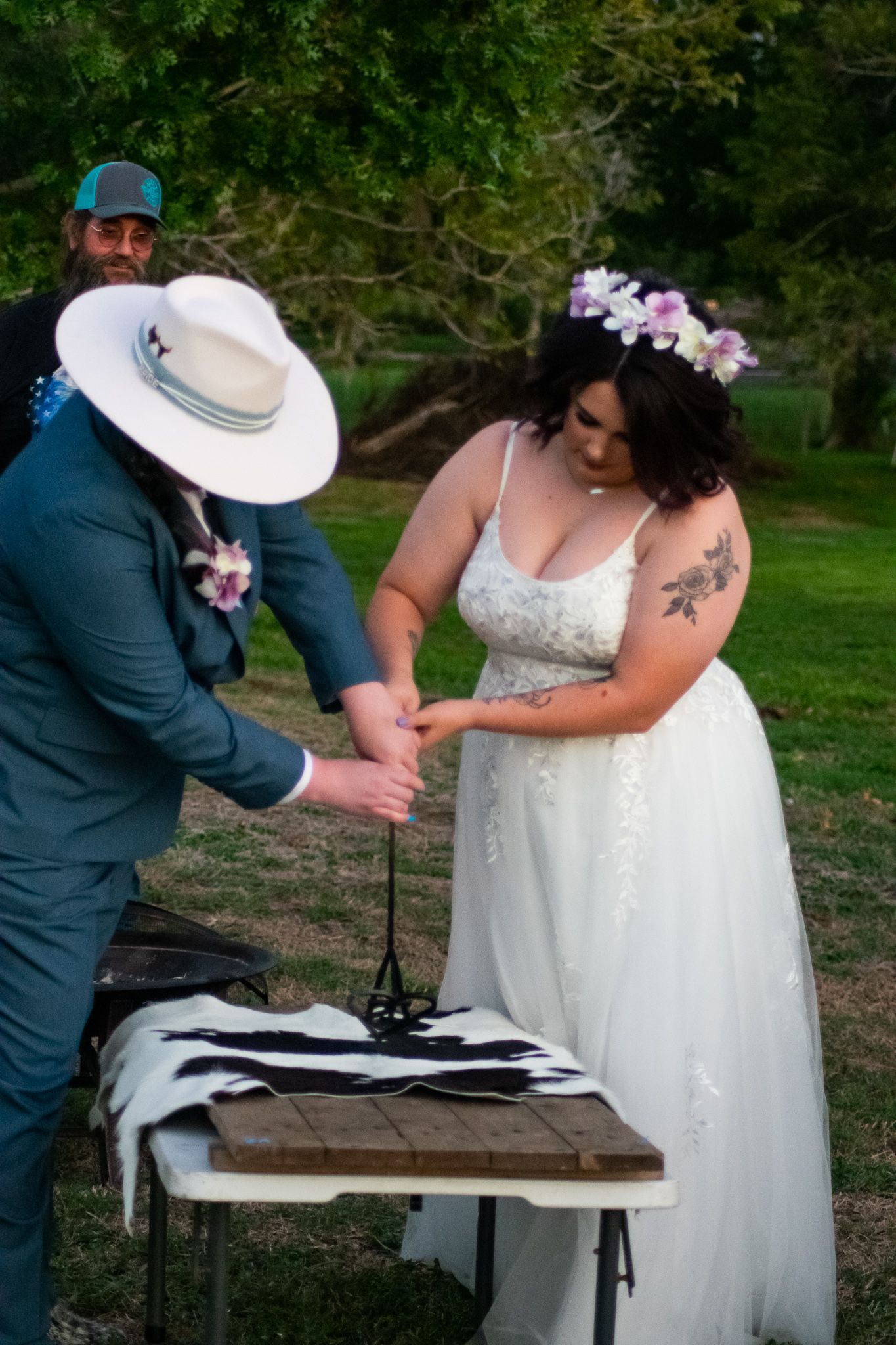 A wedding couple participates in a unity ceremony at a rustic wooden table outdoors.