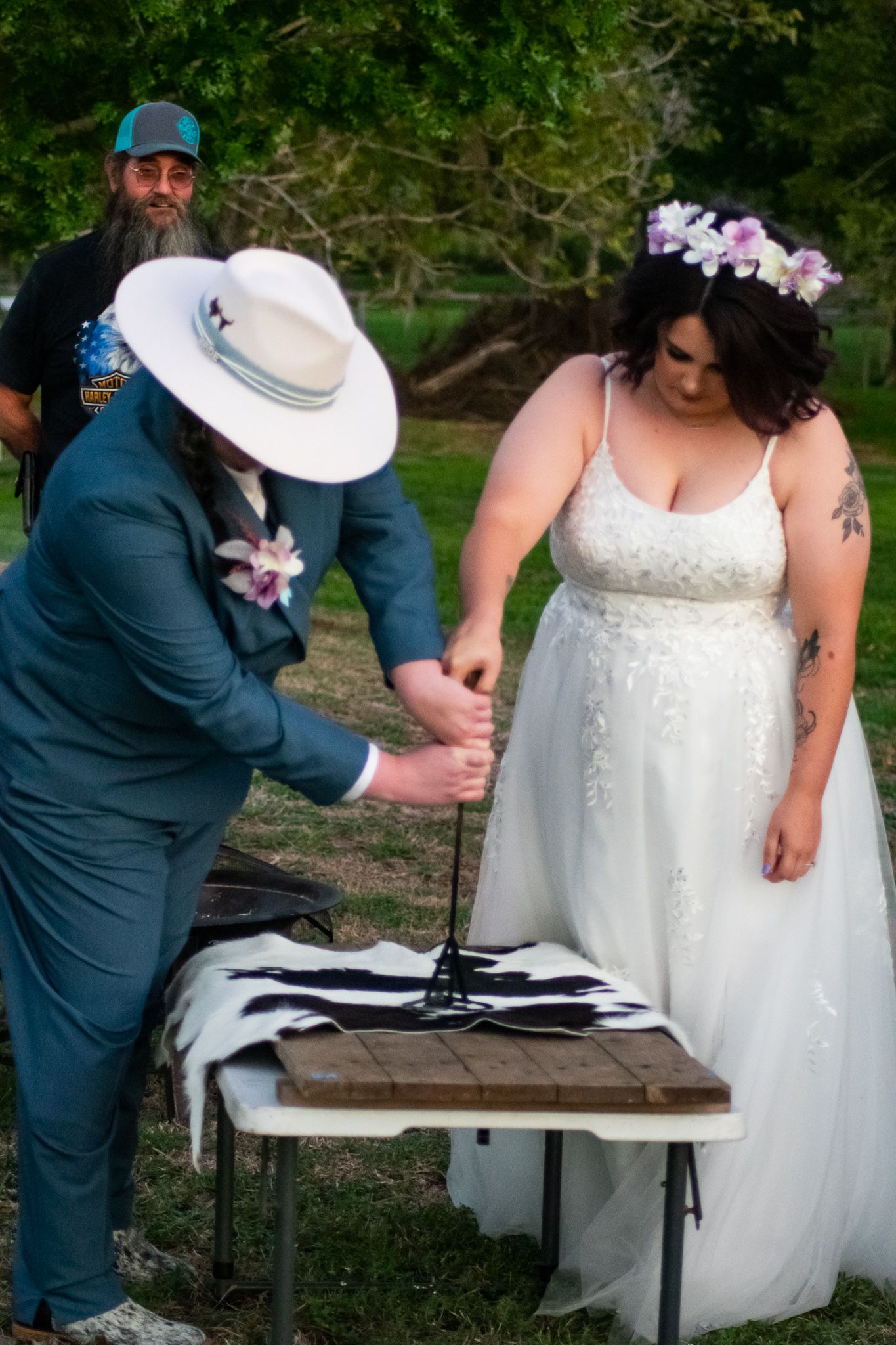 Outdoor wedding ceremony features couple performing traditional unity ritual at wooden table.