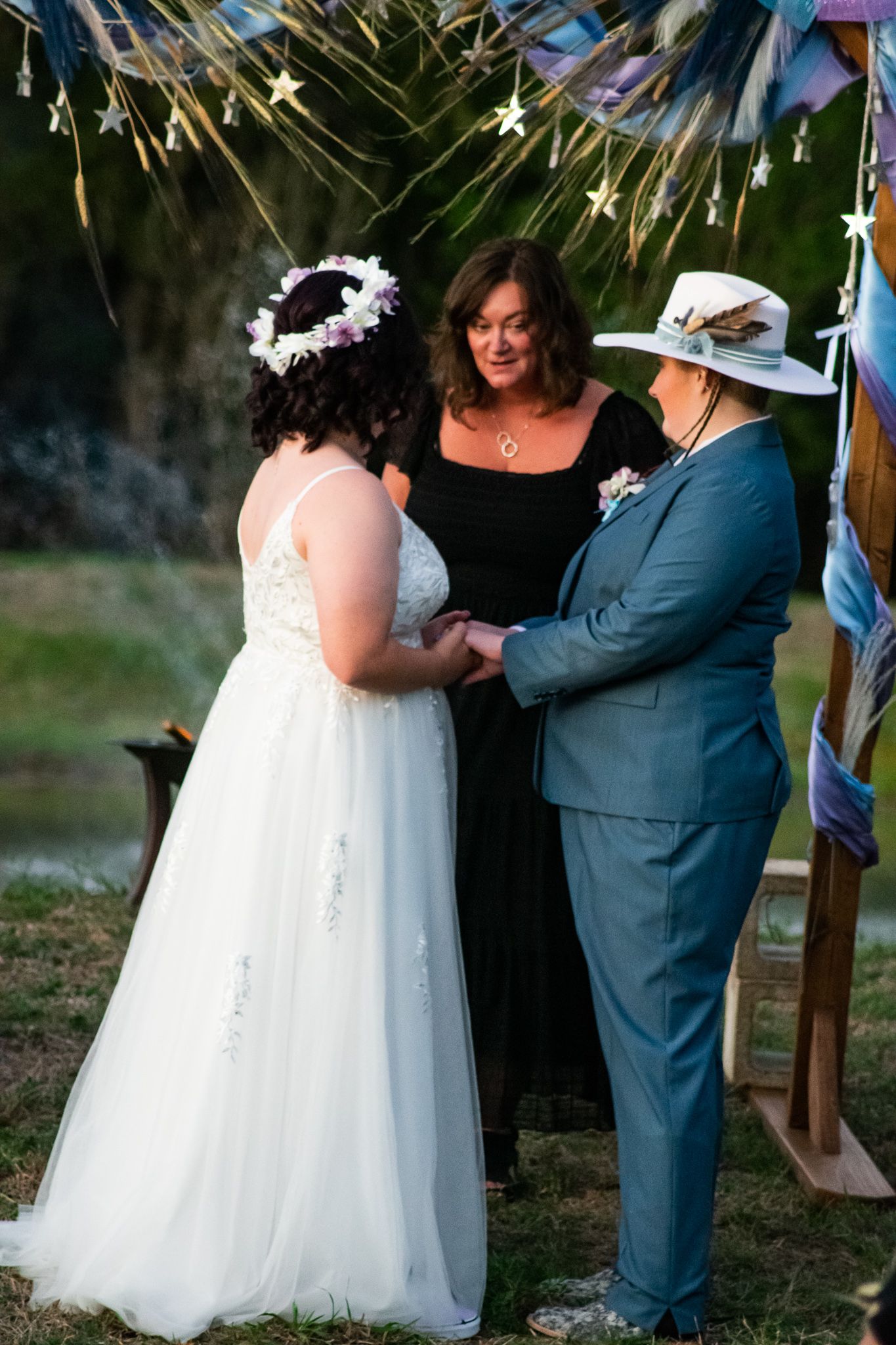 Outdoor wedding ceremony under string lights with officiant and couple exchanging vows.