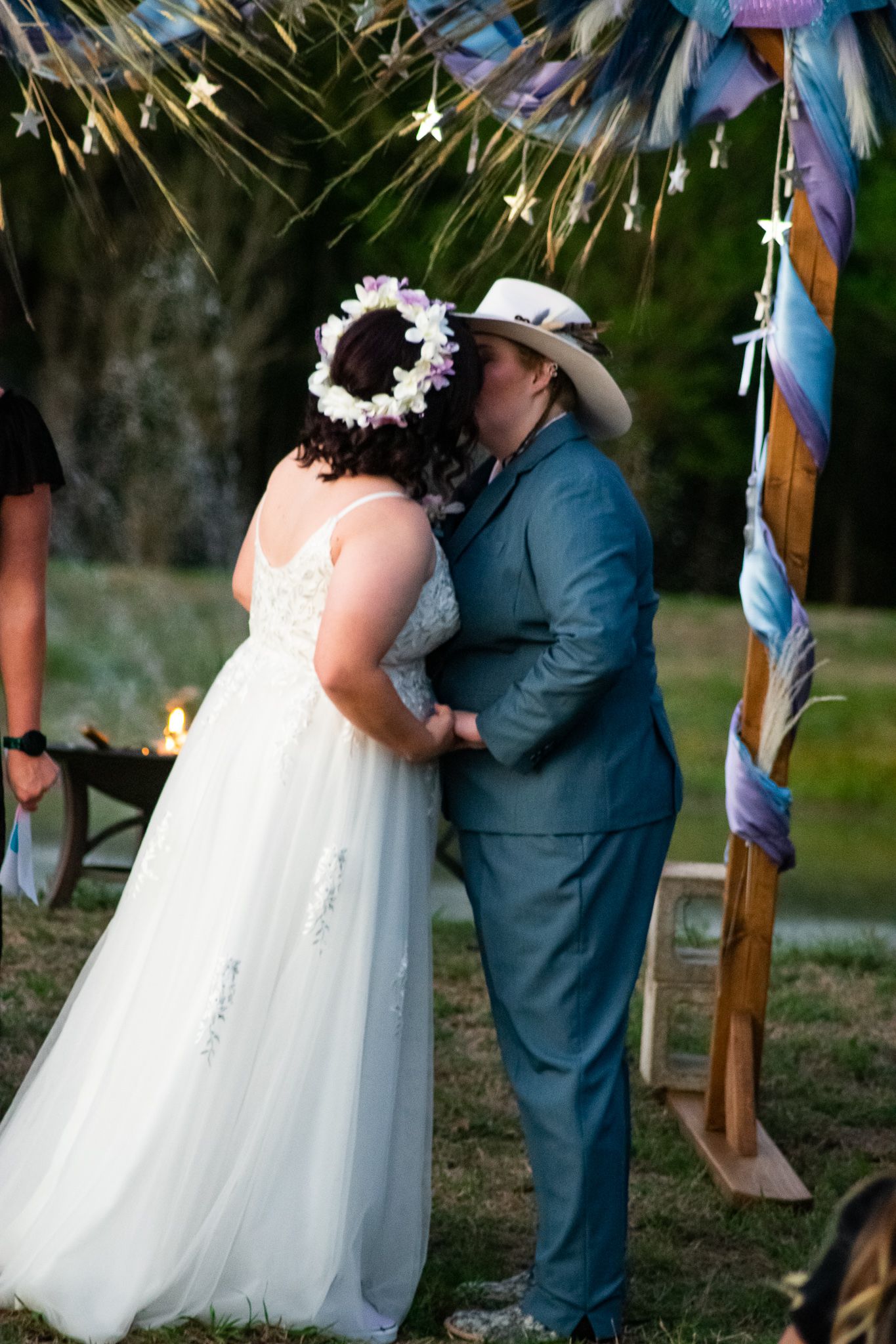 Intimate moment shared between couple during outdoor wedding ceremony under decorative lights.