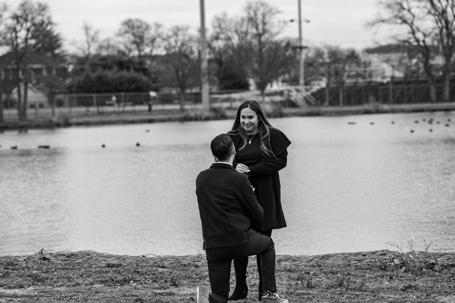 Black and white proposal moment by a lake with ducks in the background.