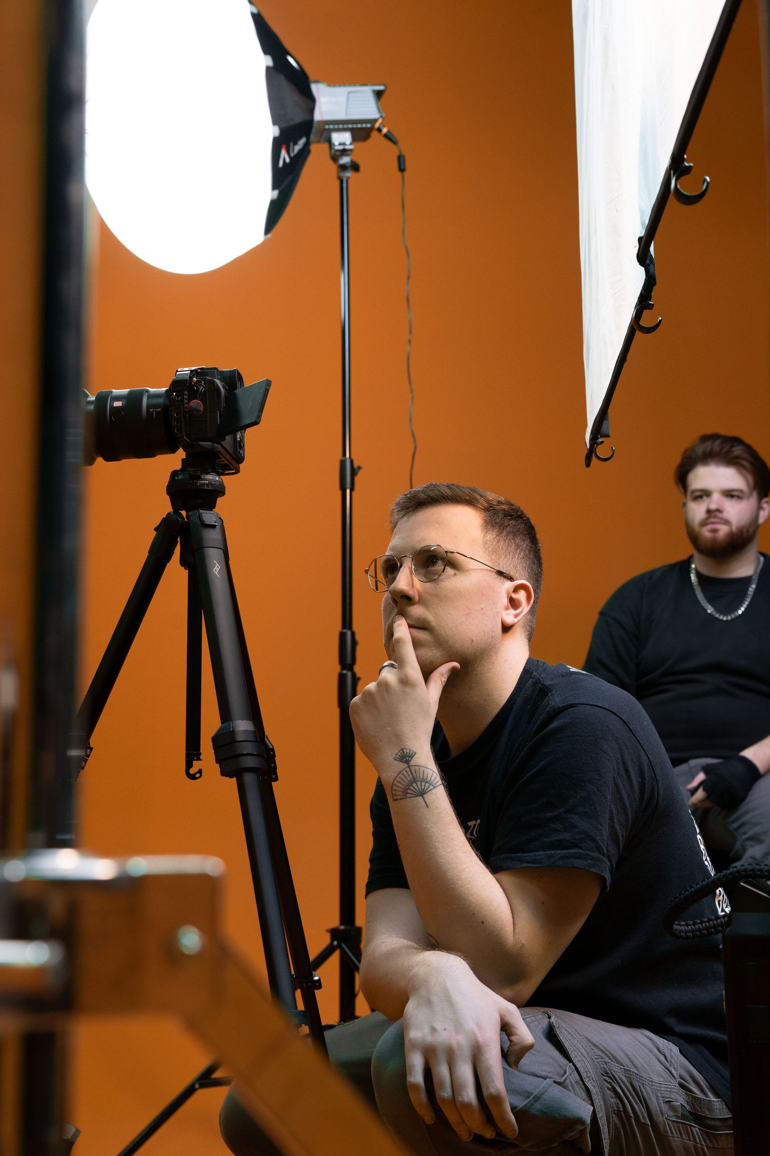 Professional photo studio setup with lighting equipment and crew members working against an orange backdrop.