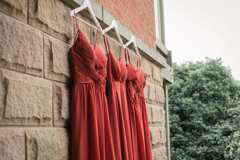 Row of coral bridesmaid dresses hanging against stone wall exterior.