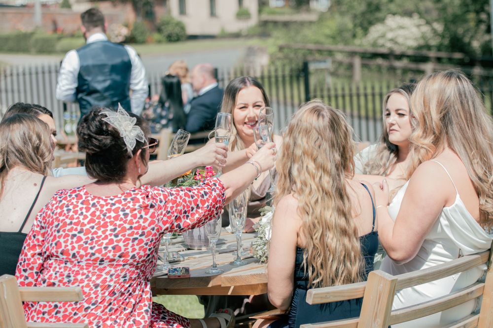 Wedding guests enjoying drinks and laughter at an outdoor reception table.