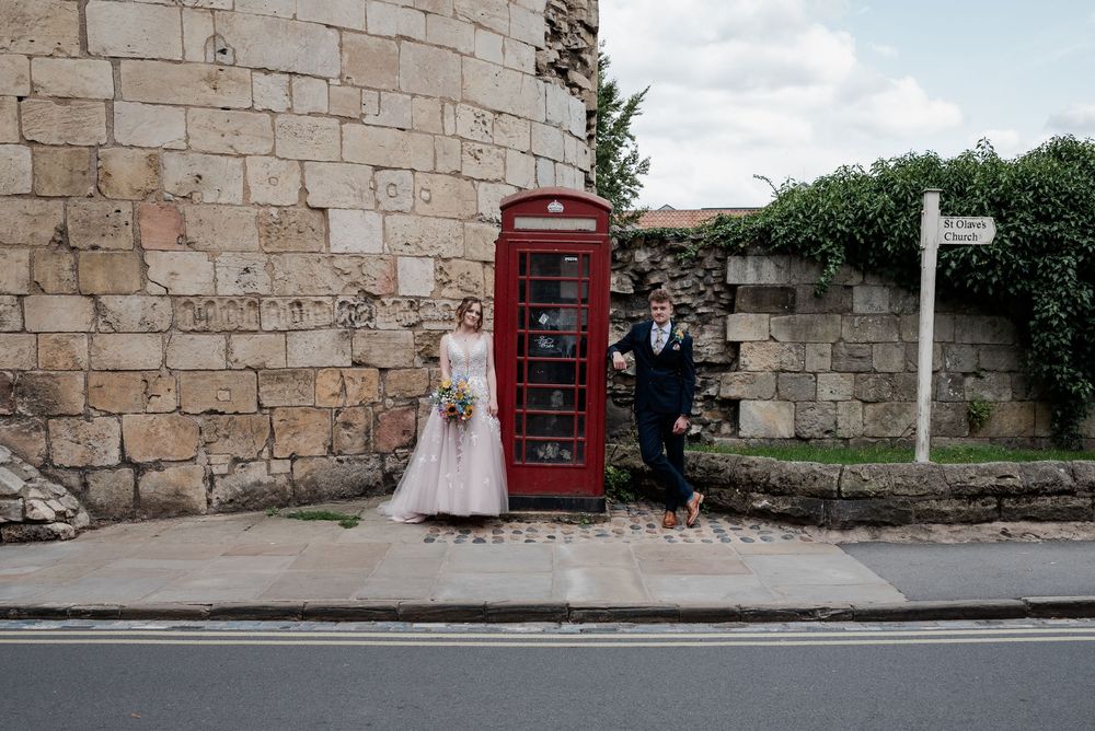Stone wall backdrop with red telephone booth visible in wedding venue setting.