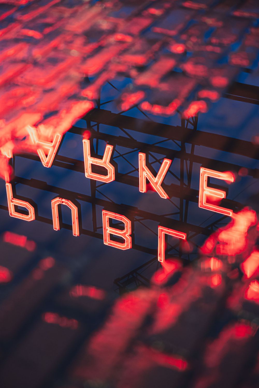 Red neon letters of the Pike Place Market sign glowing against a dark background with dramatic lighting and reflective surfaces