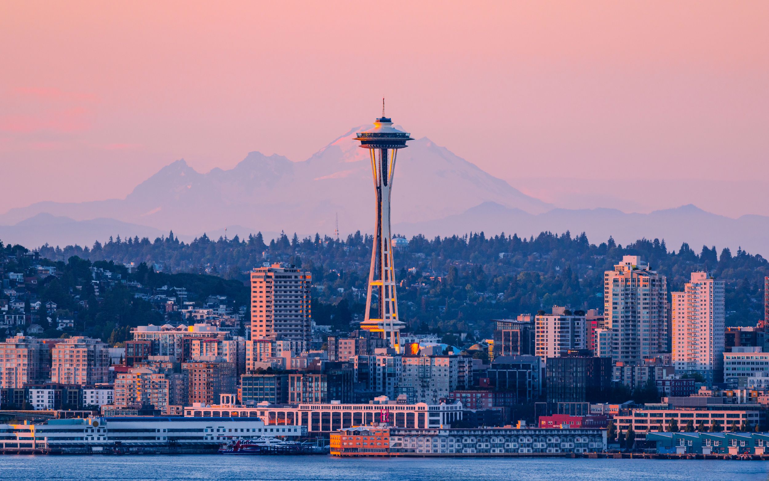 Seattle's iconic Space Needle towers over the city skyline at sunset with Mount Rainier visible in the distance.