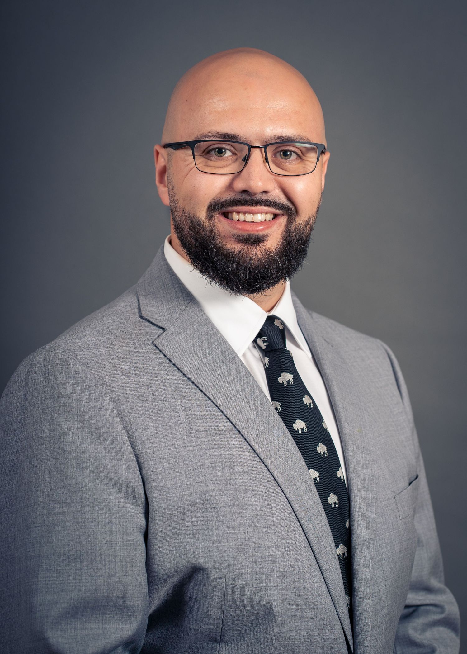 Alex Crinzi, portrait and landscape photographer, in a grey suit against a dark studio backdrop
