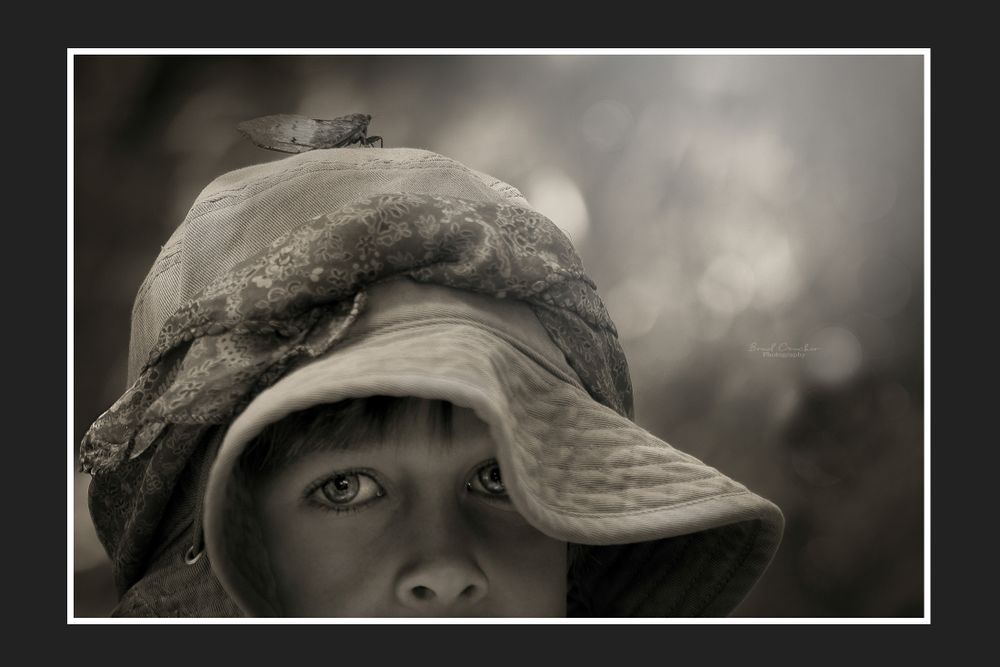 A moody black and white portrait showing eyes beneath the brim of a weathered hat.