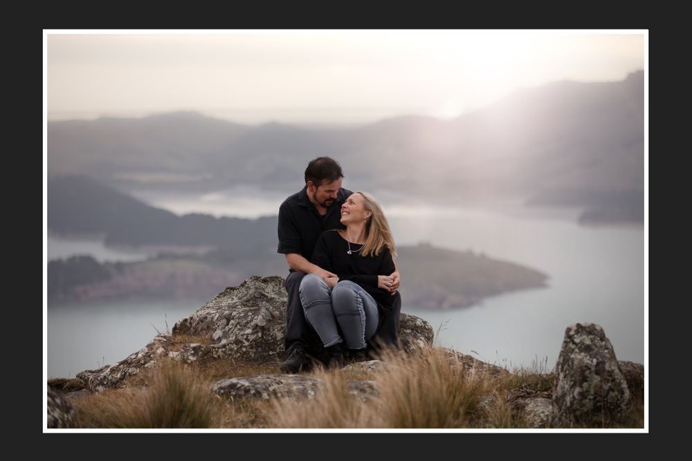 Couple sharing tender moment on mountain peak overlooking misty lake landscape.