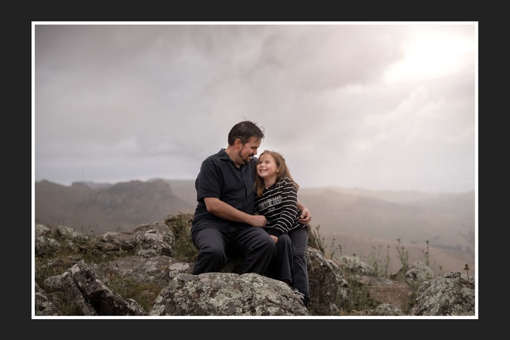 A romantic couple sits together on a rocky mountaintop overlook on a moody overcast day.