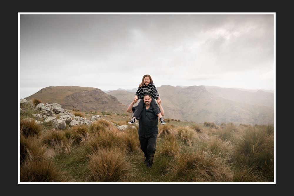 A couple hiking in the mountains with one person carrying the other on their shoulders.