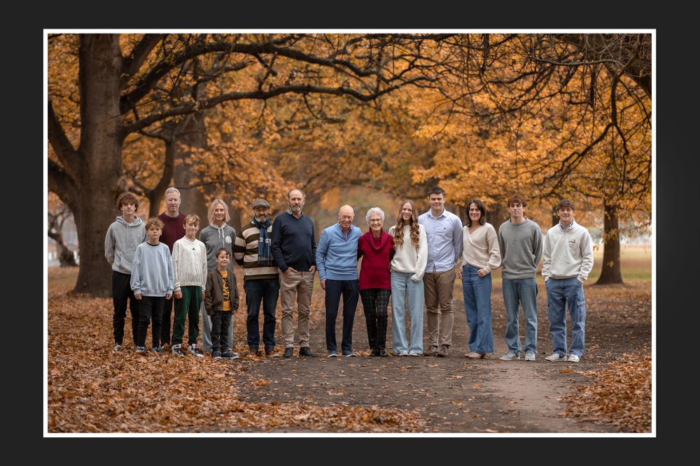 Large group poses together for outdoor portrait in fall setting with orange foliage.