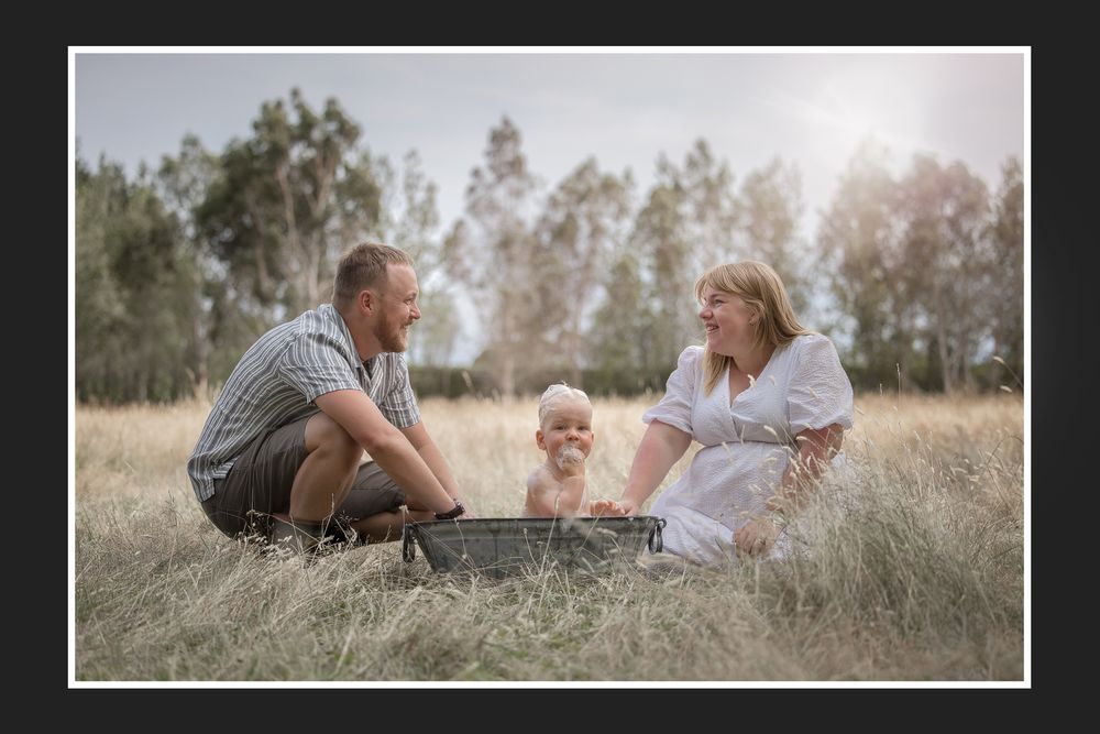 Family enjoying a relaxing summer day together on a grassy field with trees in the background.
