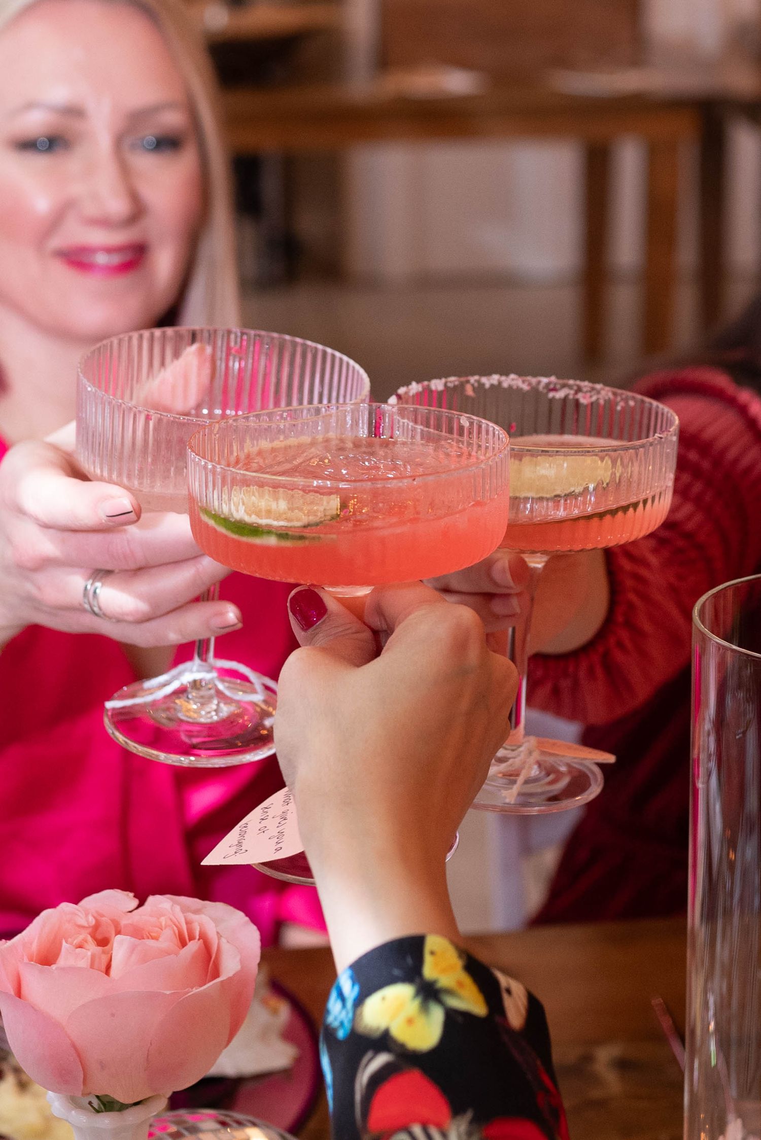 Friends toasting with pink cocktails at a celebratory gathering with floral decorations.