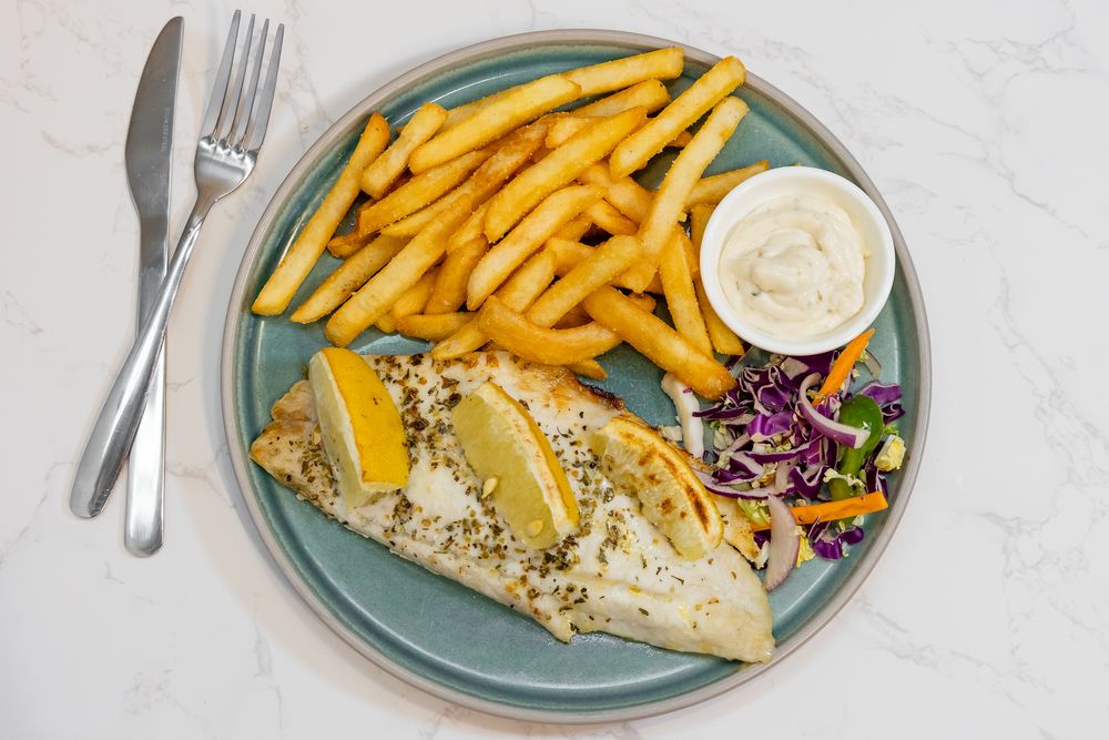 Fish and chips plate with coleslaw and tartar sauce on blue ceramic dish.