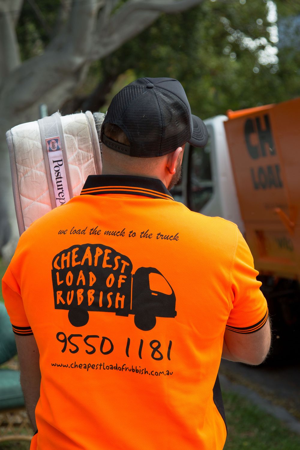 Worker in bright orange t-shirt with 'Cheapest Load of Rubbish' text and truck logo carrying materials.