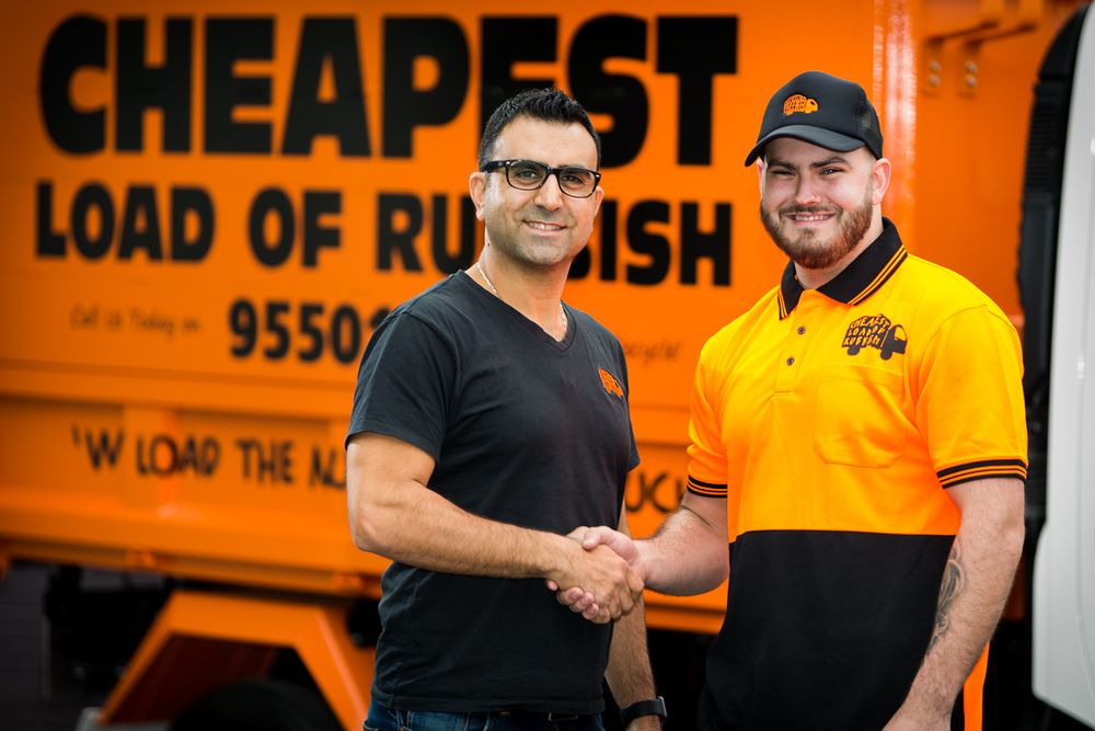 Two men shake hands in front of an orange waste management truck.