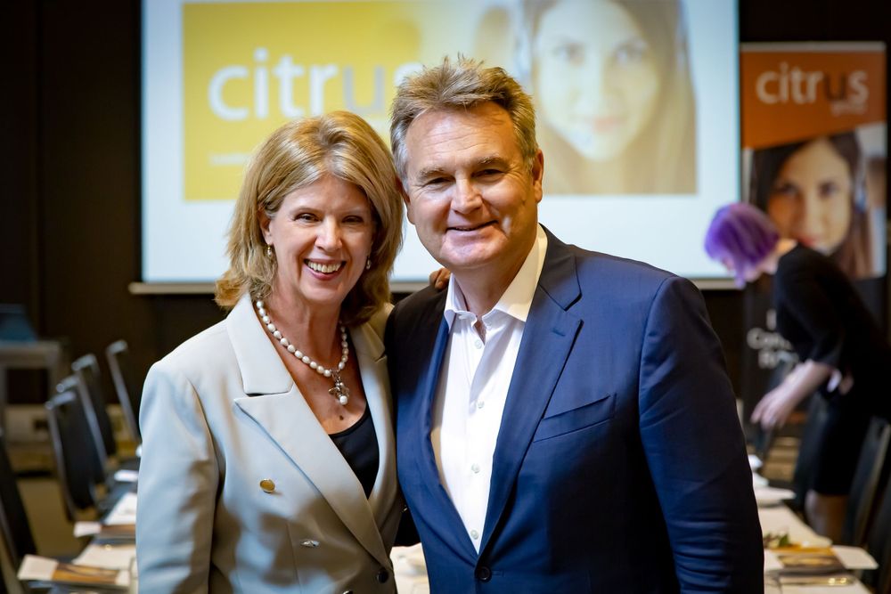 Sydney Event Photography - Two people pose at a corporate event with branded backdrop and presentation screens.
