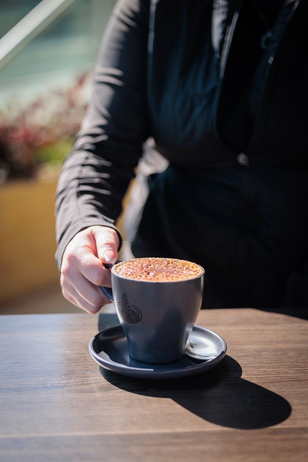 Hand holding a cappuccino cup with latte art on wooden table surface.