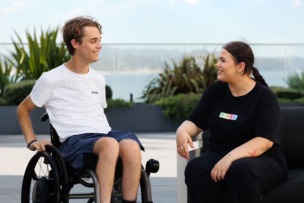 Two people engage in conversation on an outdoor patio with ocean views.