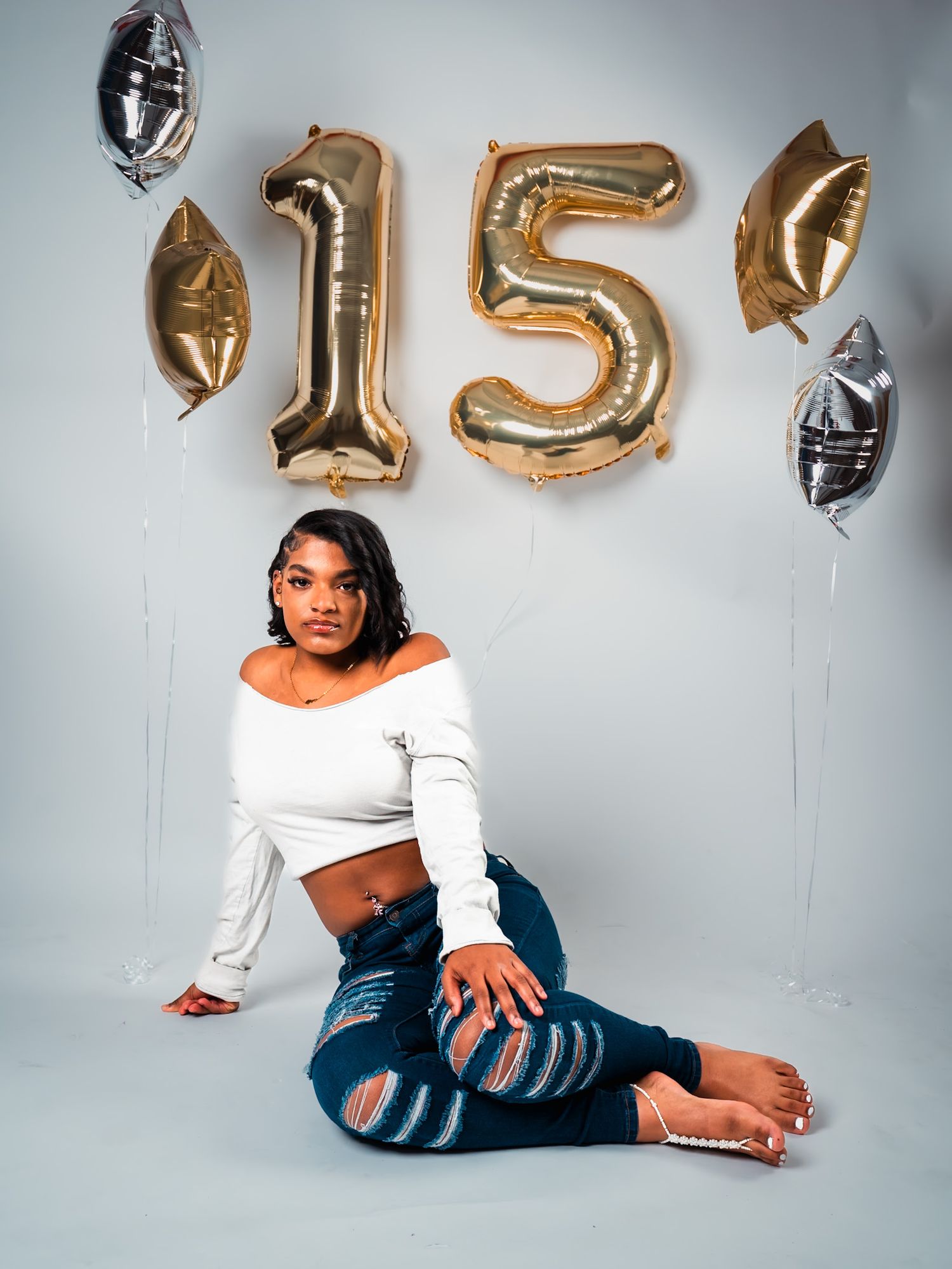 Birthday party setup with gold number 15 balloons and silver football balloons against white wall for quinceañera celebration.