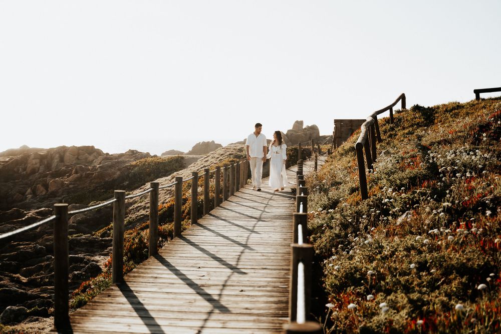 A couple walking along a wooden boardwalk on a coastal path during sunset.