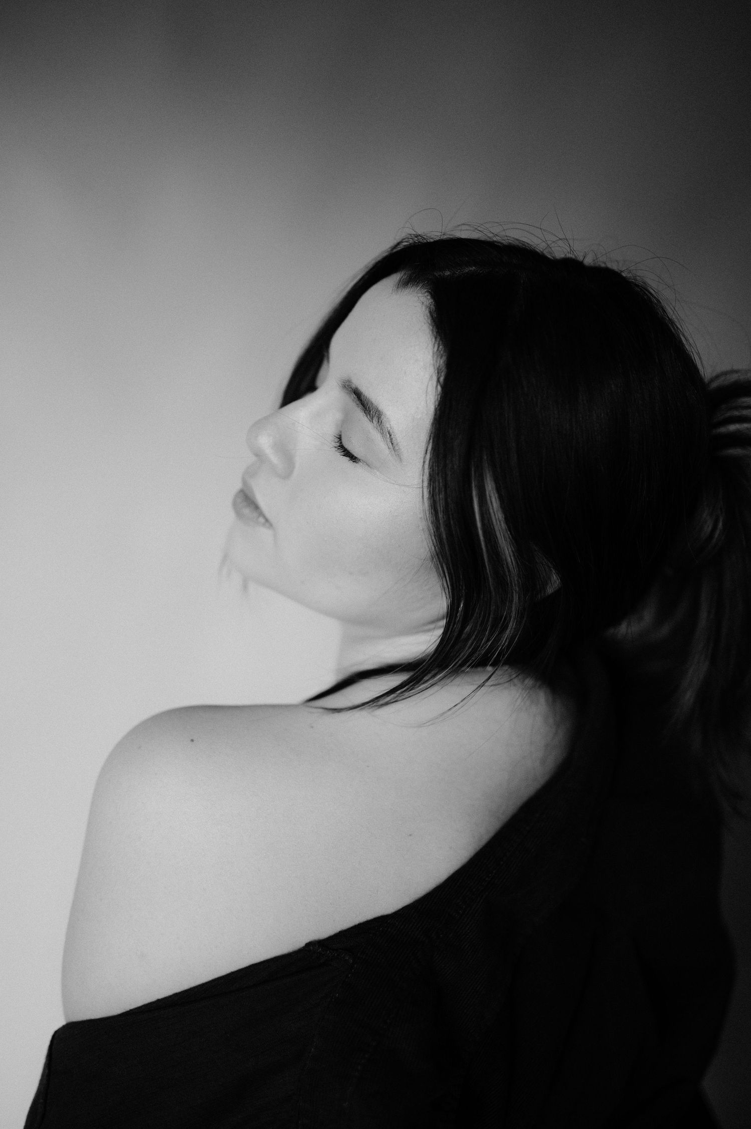 Artistic black and white portrait showing an off-shoulder pose with dramatic side lighting.