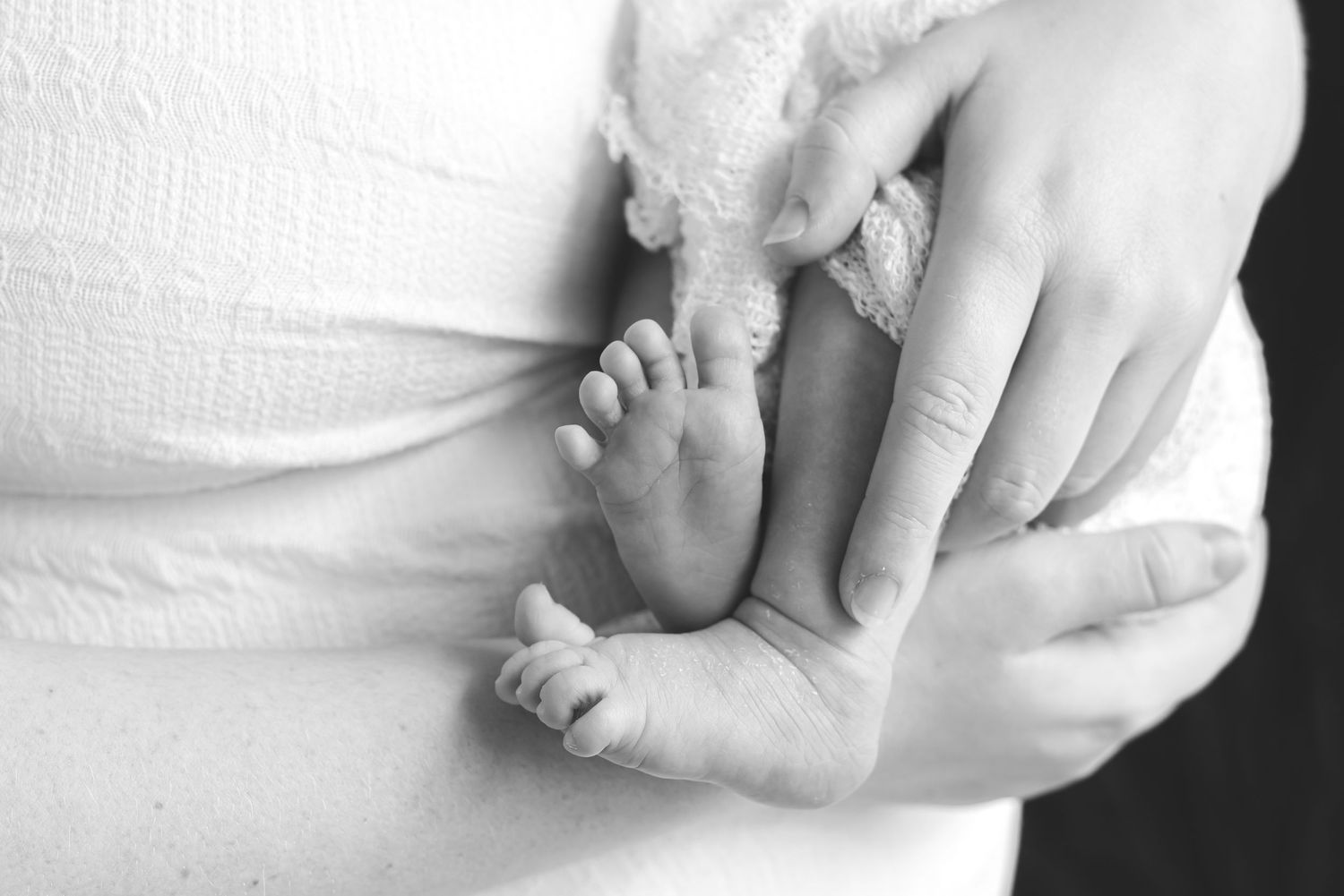 Close-up black and white photo of tiny newborn feet being gently held.