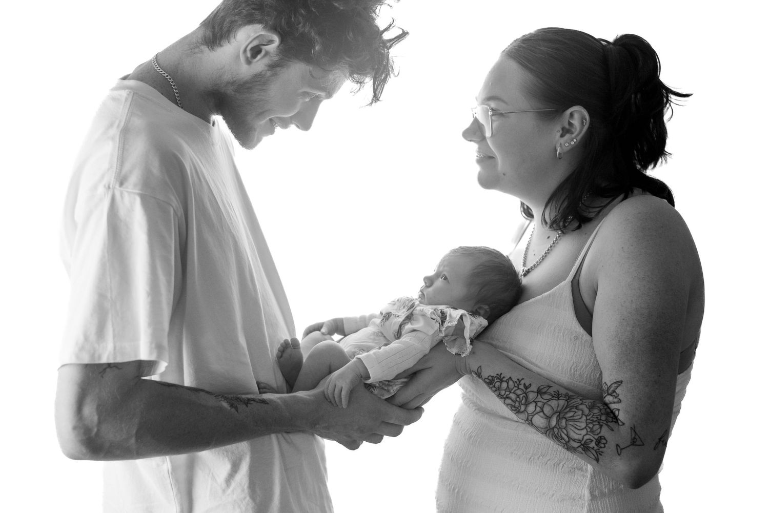 Black and white photo of a couple tenderly holding their newborn baby together.