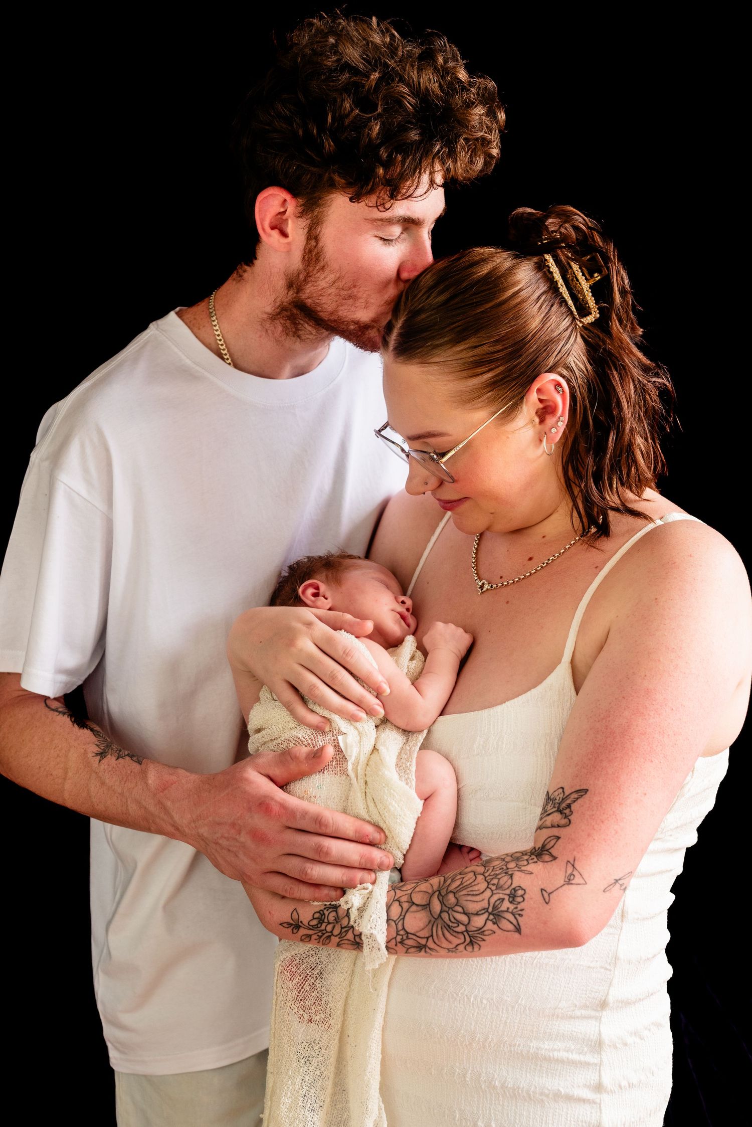 Intimate family portrait with new parents holding their infant against a dark background.