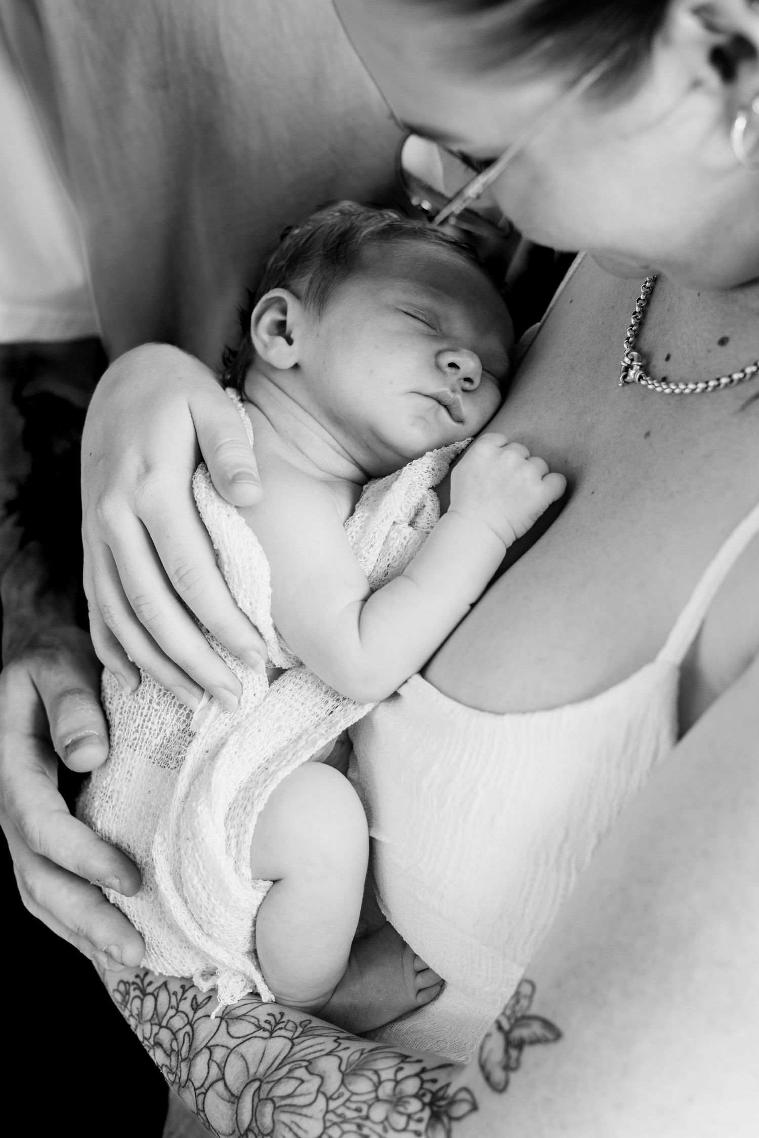 Black and white image of sleeping newborn being held against parent's chest.