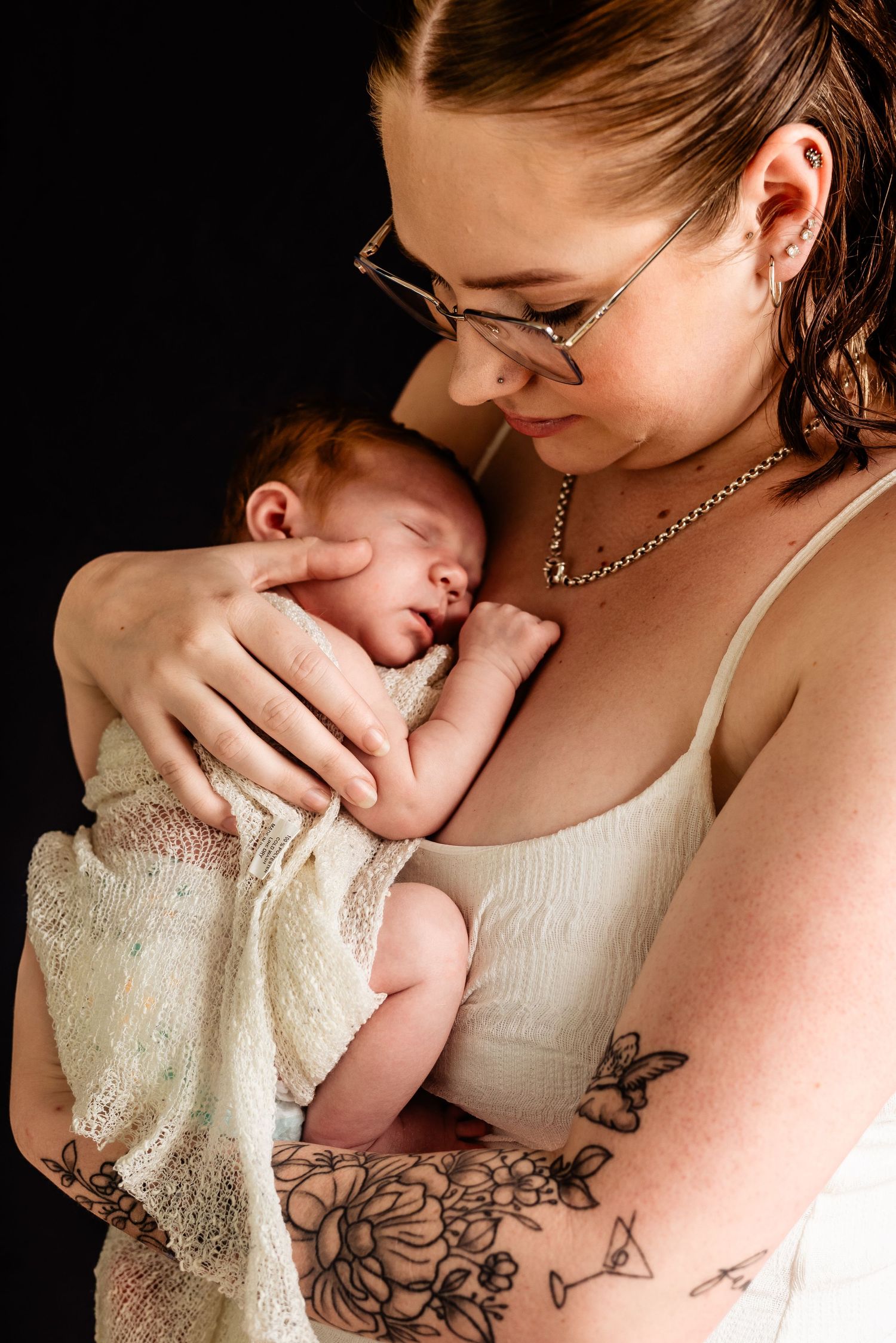 Close-up portrait of parent cradling newborn baby wrapped in lace blanket against dark background.