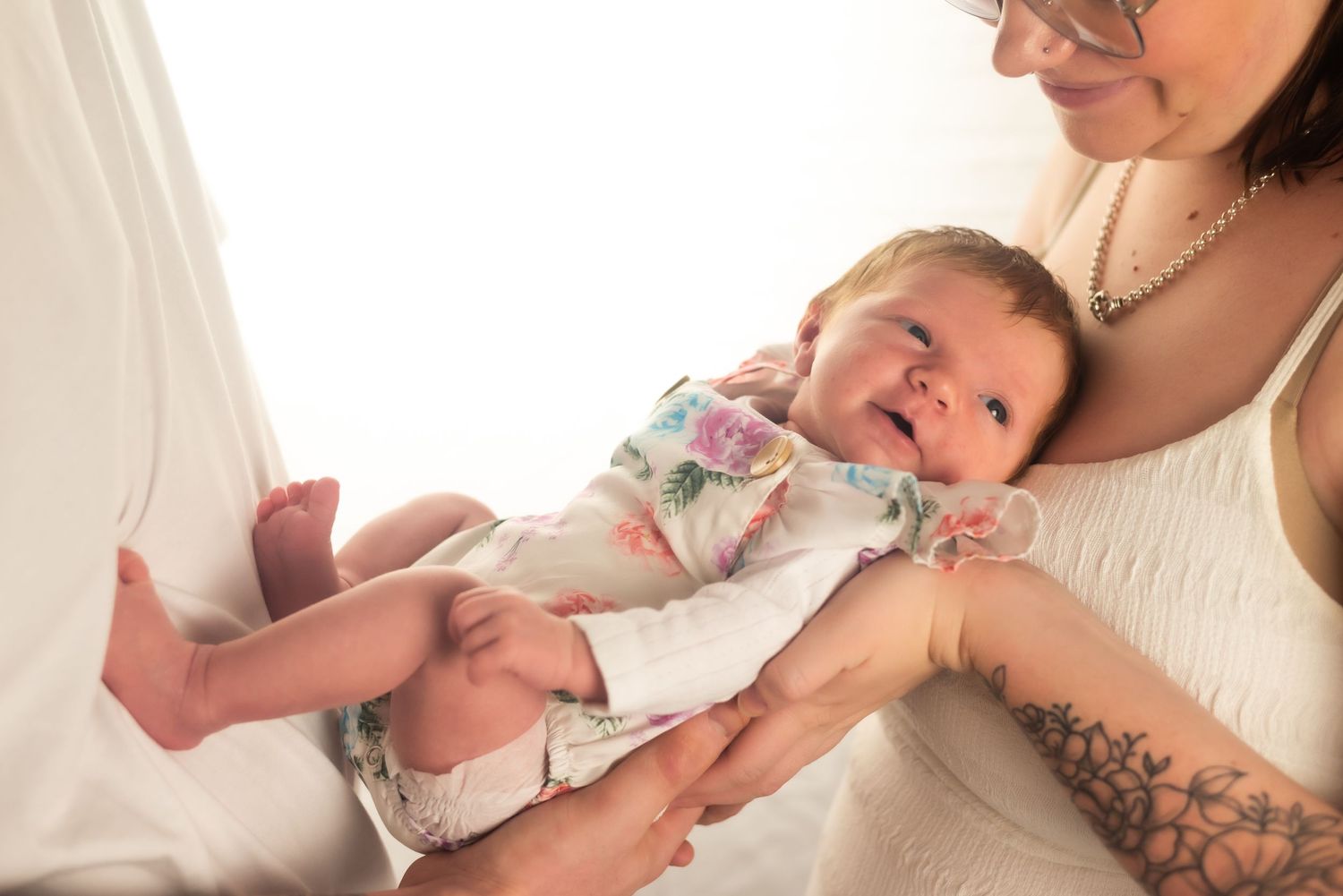 Parent holding smiling baby wearing floral outfit in bright setting.