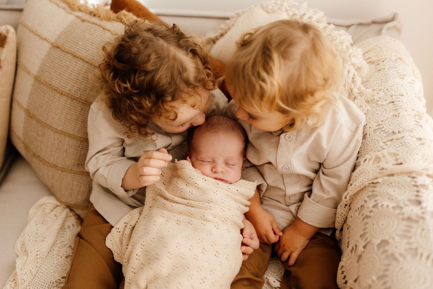 Three siblings snuggling together on a cozy couch.