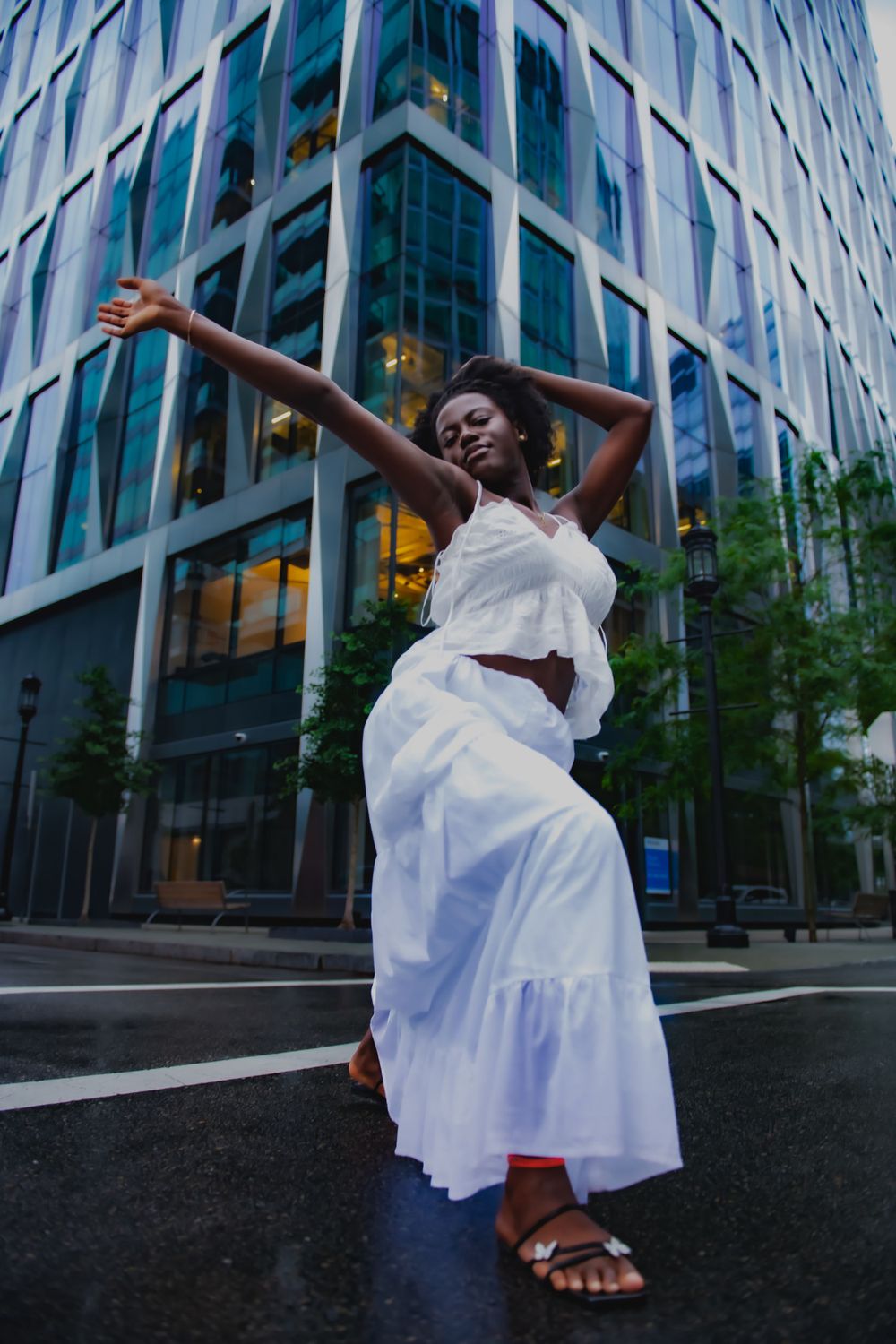 Expressive dance movement in white dress against modern glass building architecture.