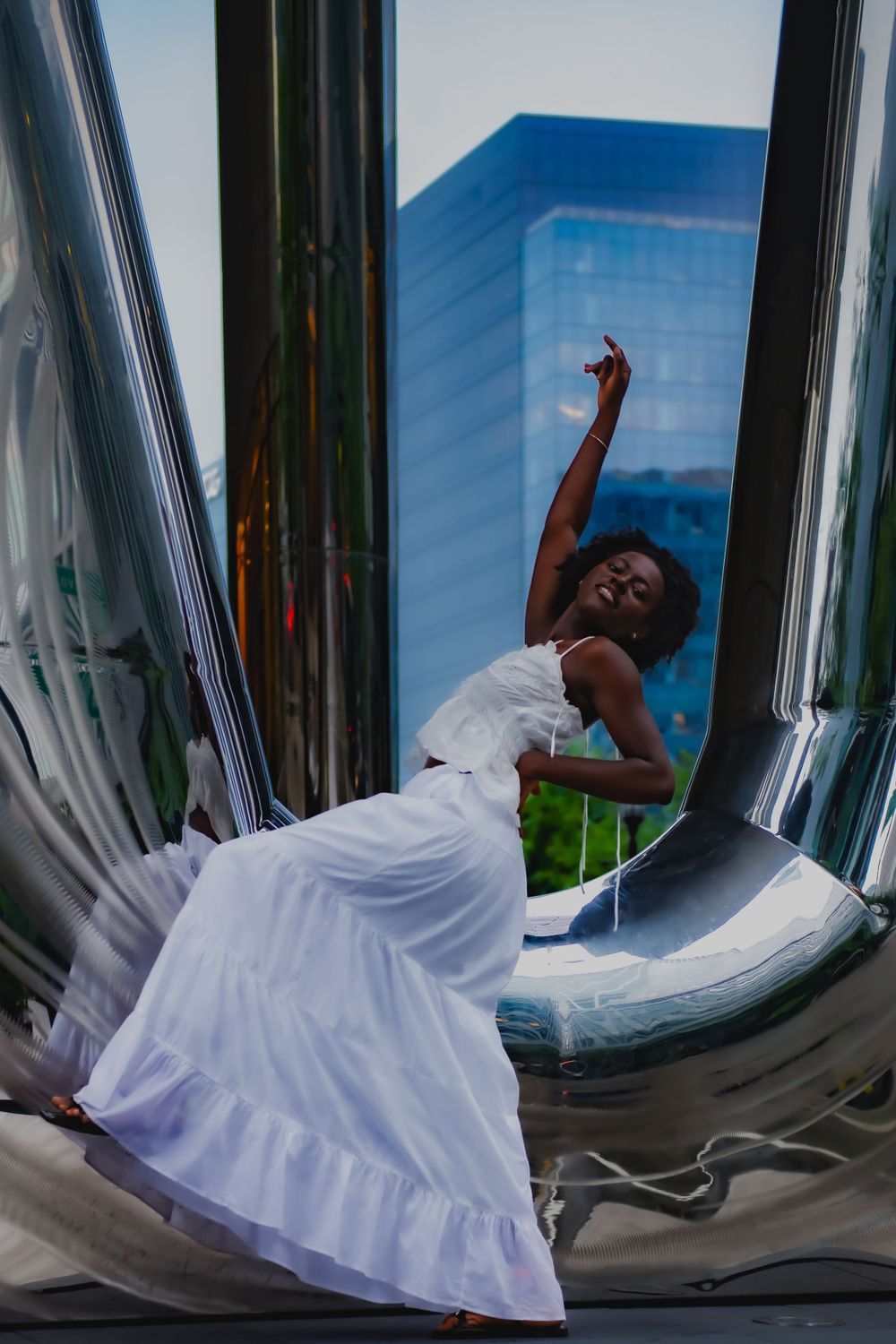 Artistic portrait in white dress against reflective urban architecture.
