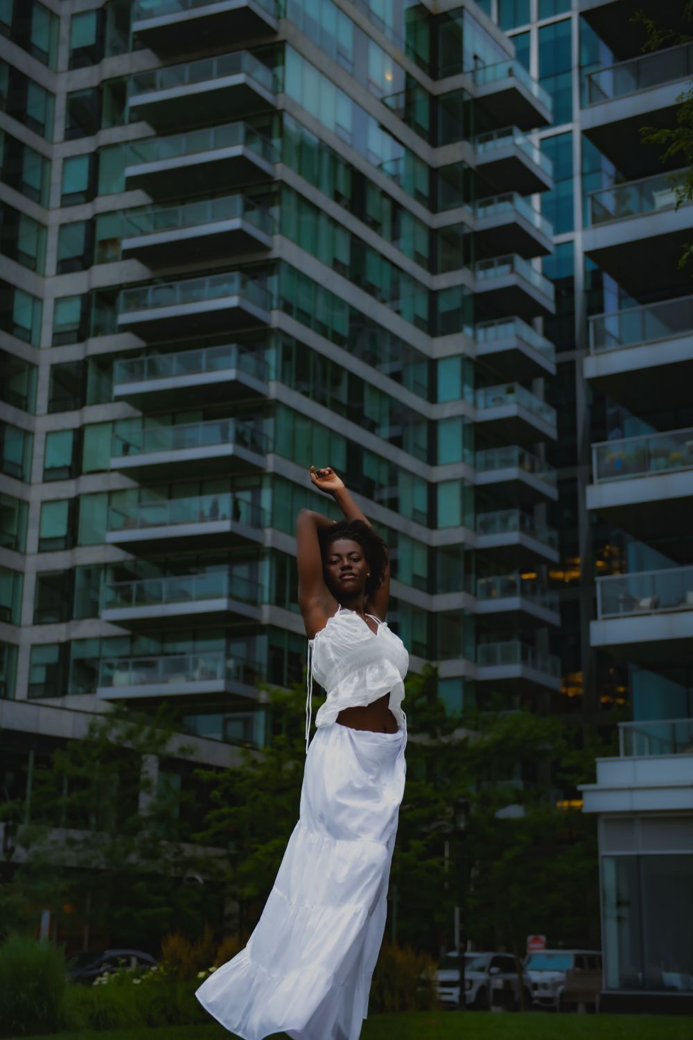 Elegant dance pose in white dress against modern high-rise buildings.